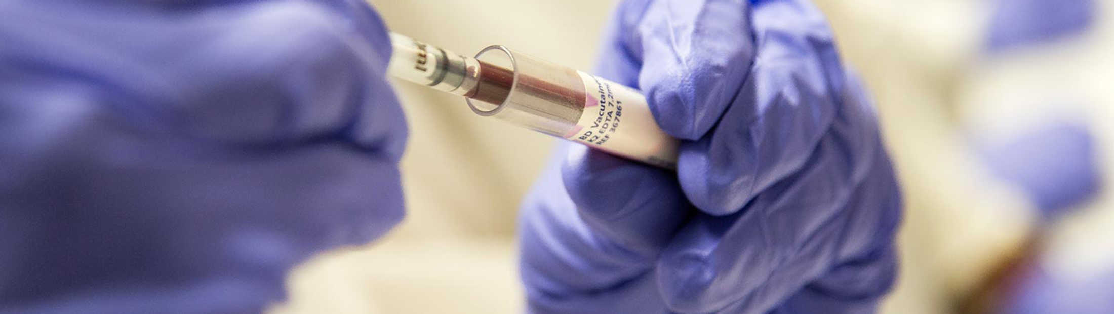 A person pipetting blood into a vial.