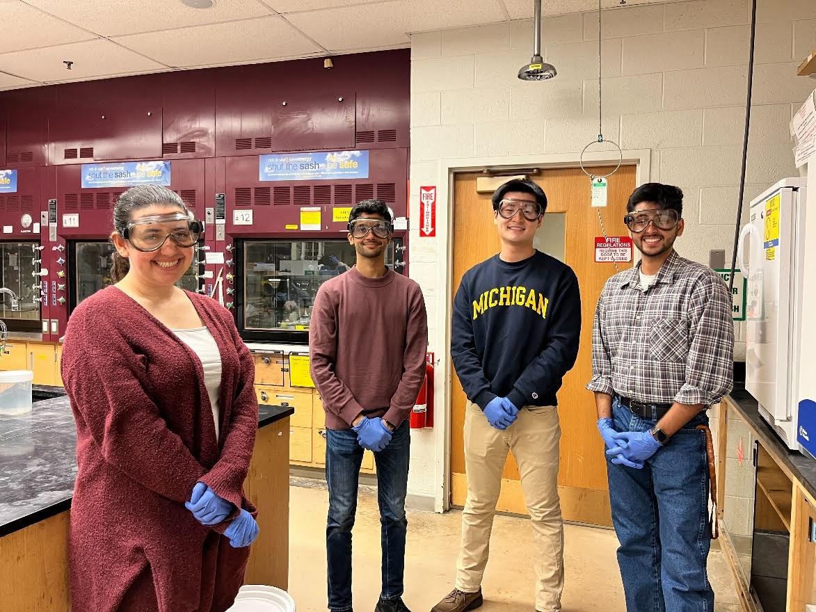 Four graduate students stand in lab wearing safety goggles.