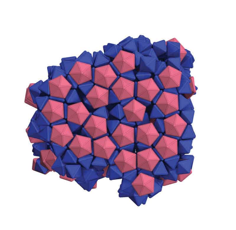 Blue octahedra and pink decahedra cram together in a roundish cluster, which is just a cross section of a larger structure. In some places, the pink particles line up well with the blue particles along the outer surface of the structure. More internal layers are visible based on the pink particles. In these layers, the faces of the blue particles don't perfectly align, creating some black, empty space.