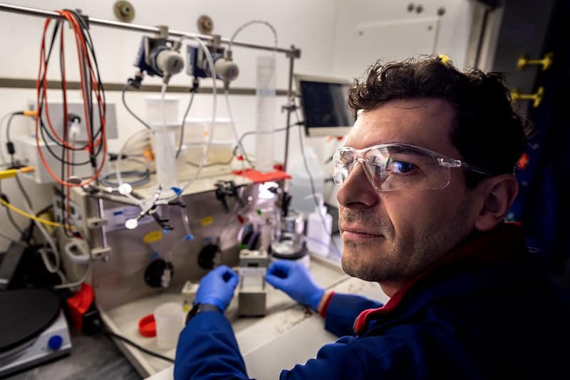 Jovan Kamcev conducting research under a hood while looking at the camera